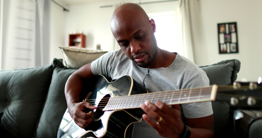 Black man practicing guitar at home. African mixed race learning to play musical instrument
