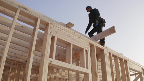 View from below of a worker against the sky. A laborer is working at the frame house building site, adjusting wooden planks