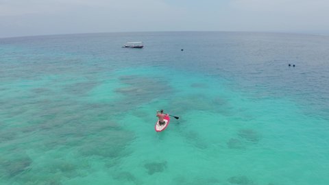 Aerial view of young man tourist floats on red boat on clear azure waters on a warm summer day while relaxing on a tropical island. Boating and diving concept