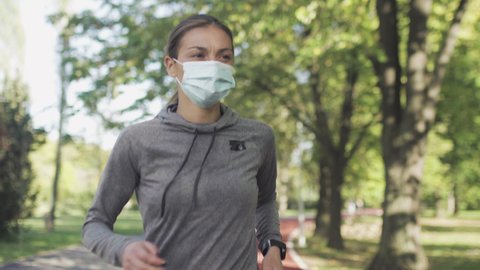 Fitness girl running on an all weather synthetic track surface in the park. Wearing protective face mask. Sport during pandemic.