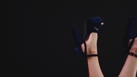 elegant female feet in stiletto heels waving and swinging on black background