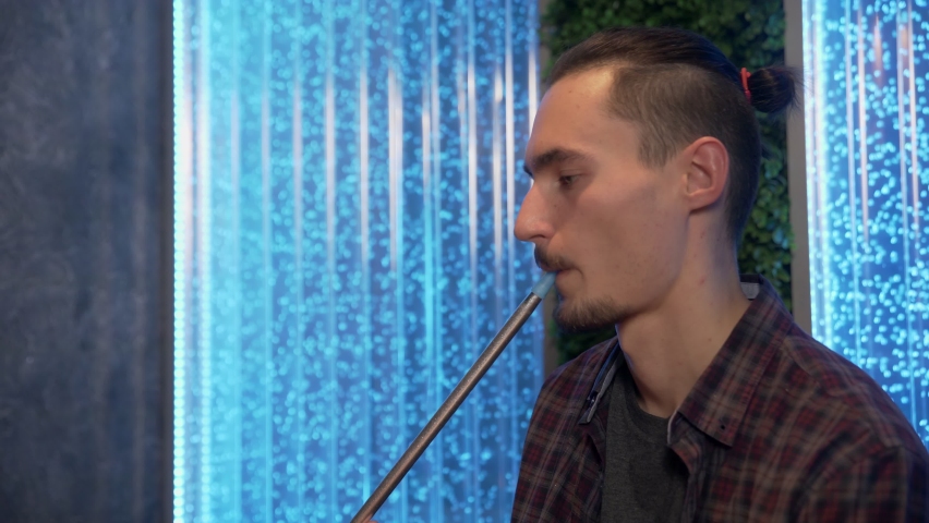 Close up of man smoking traditional hookah pipe and making smoke clouds in a form of rings.