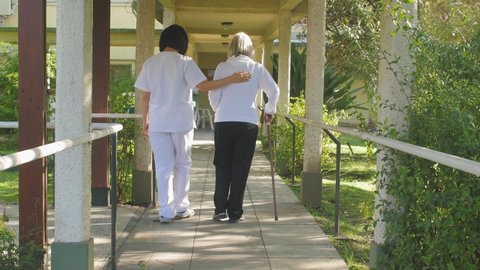 Asian Doctor helping caucasian elderly woman with walker in the garden