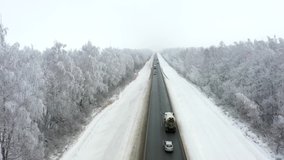 Aerial video flying over a winter paved straight road with cars driving along the road there are beautiful trees covered with frost