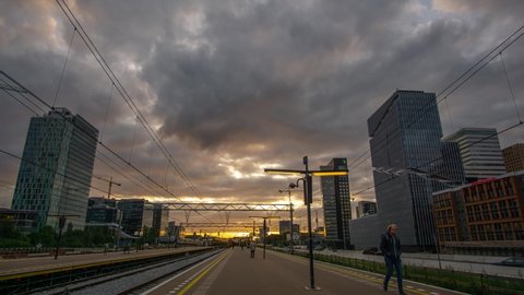 Amsterdam, the Netherlands - october 17th 2019: Time lapse of rush hour at the Amsterdam Zuidas train station with cars and trains passing by and commuters walking from the platform to work in offices