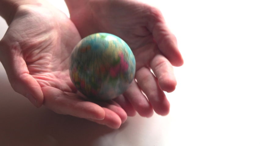 A mini copy of a globe lies in the hands closeup. The hand or hands are playing with a small blue globe. Wanderlust, pandemic, border closures.