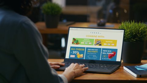 Person Uses Laptop Computer Browsing through Online Food Delivery Market, Choosing Through Vegetables Section, Fresh Goods. Internet Store Software with List of Food to Order. Over The Shoulder