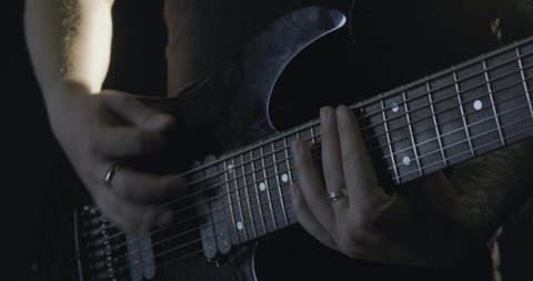 Young male with tattoos play on the guitar in black studio