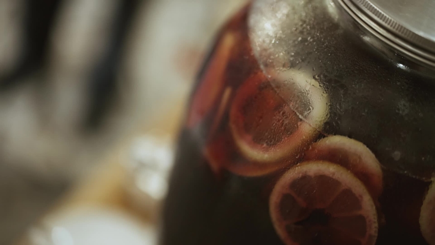 Close-up, condensation, drops on a large glass transparent jar with a metal lid with cold fruit lemonade with slices of citrus oranges
