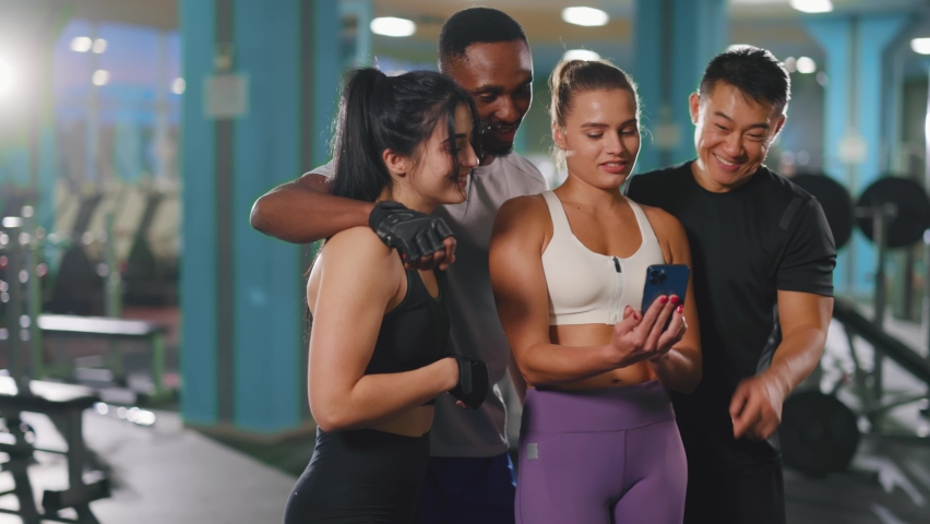 Attractive multi-ethnic diverse group of four amazing friends men and women using mobile phone after workout. Technology. People and sport. Friendship. | Shutterstock HD Video #1064731804