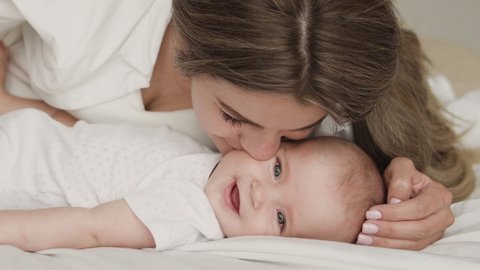 Young woman kissing adorable baby, playing with newborn, parent affection, love