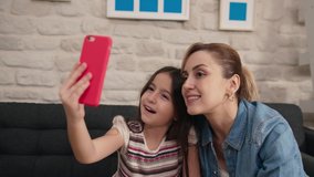 Little girl and mother talking on video conference by smart phone with happiness and smile together in living room at home. 