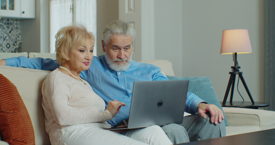 Old retired couple using laptop doing internet shopping choose sale offers together, senior elderly family grandparents relaxing looking at computer screen sit on sofa at home. Coronavirus quarantine | Shutterstock HD Video #1064742097