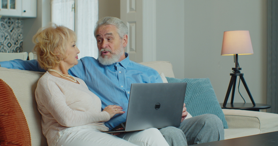 Old middle aged couple using laptop talking together doing online shopping, senior mature retired family reading discussing internet computer news. Coronavirus quarantine lockdown. | Shutterstock HD Video #1064742103