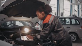 Handheld shot black female auto mechanic in uniform typing on laptop lying under hood of car and using tool to make repairs - Powered by Shutterstock - Get 15% off with code: PIKWIZARD15