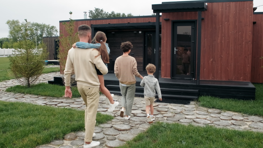 Slowmo tracking of father holding 8-year-old girl and mother holding hand of little boy walking towards their house