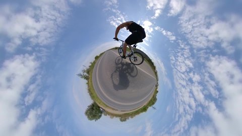 Bicycling. View of a small planet. 360 degree camera.
The cyclist rides fast on the highway. Around the planet is the sky with clouds.