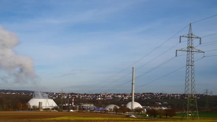 Nuclear power plant in Neckarwestheim, Germany, located at the bank of Neckar river, with power line, pylon and blooming agricultural field with yellow rapeseed flowers in front in fall season.