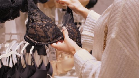 Professional designer holds black and brown lacy bra and hangs back on wall with underwear range in shopping centre. Concept fashion