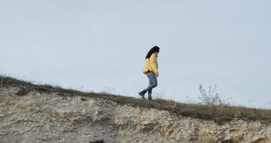 an energetic and positive girl, she runs confidently on the edge of a precipice, a rock in short yellow, at sunset. A goal to which you run at any cost. Slow motion.