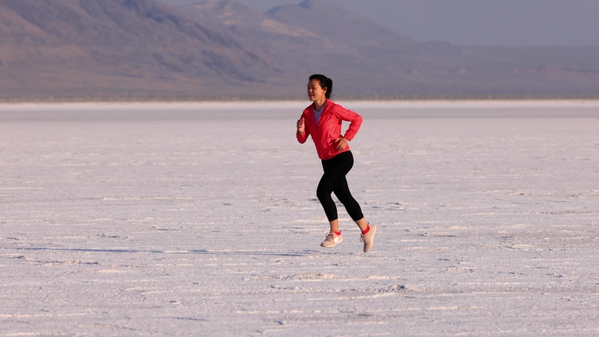 Asian woman jogging across the Bonneville Salt Flats flats in Utah. Slow Motion.
