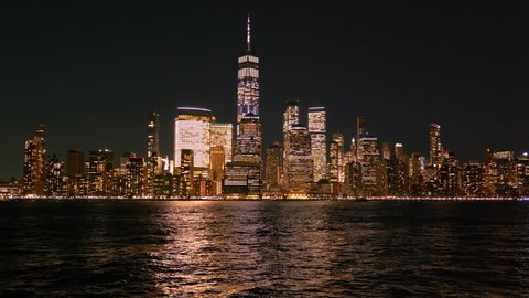 New York City skyline at night time looking across the Hudson river into downtown Manhattan with the One World Trade Center lit up.