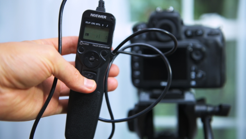 Herndon, USA - July 24, 2019: Professional photographer holding wired shutter trigger release intervalometer or remote controller that controls Dslr and mirrorless cameras | Shutterstock HD Video #1064771476