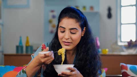 Smiling woman in her early twenties eating a bowl of freshly made hot noodles. Closeup shot of a college-goer having instant noodles at home - an unhealthy lifestyle and eating habits