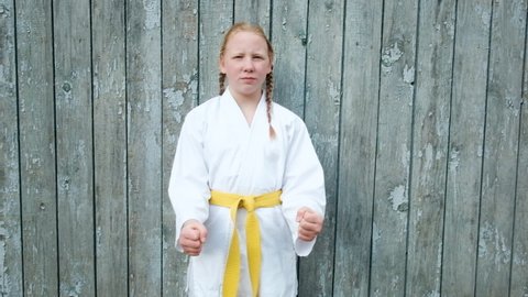 teenager girl 12 years old is engaged in karate on the background of a wooden fence. Healthy lifestyle concept. playing sports. martial arts. Judo, Jiujitsu. brave, strong, punching punches. Workouts