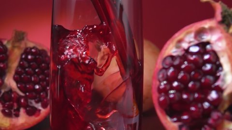 Close-up of pomegranate juice flowing into a jug on the red background of pomegranate halves in slow motion