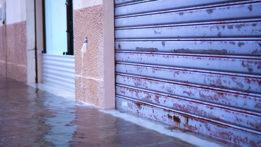 Flood water flows from small grey drain pipe on wall