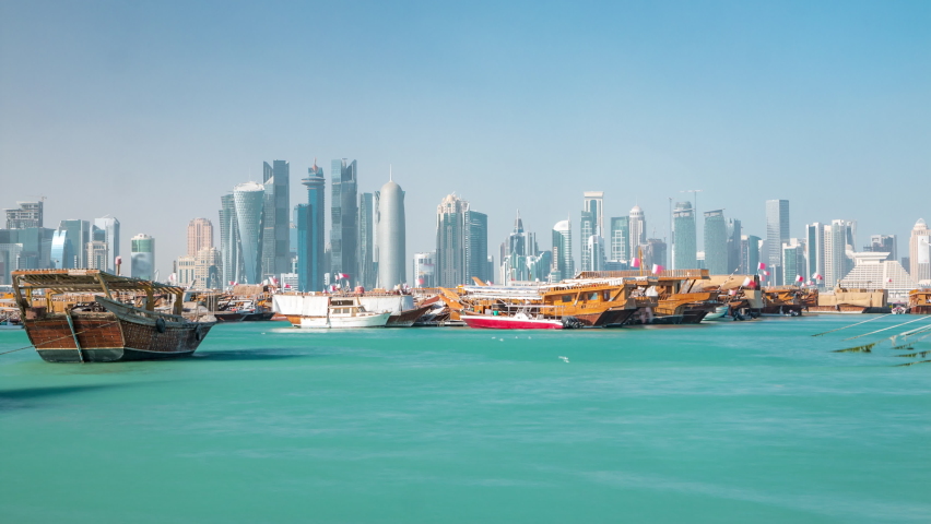 A panoramic view of the old dhow harbour timelapse in Doha, Qatar, with the West Bay skyline in the background. Modern skyscrapers on background and old boats on foreground.