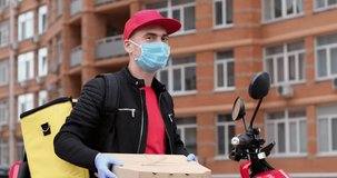 A food delivery man wearing a mask and gloves holds out two square cardboard boxes towards the video camera and shows with his hand an “OK” sign. Excellent delivery.