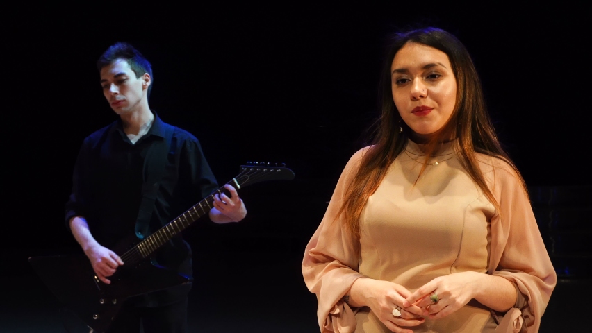 Man guitarist playing electric guitar with female singer on stage in the dark.