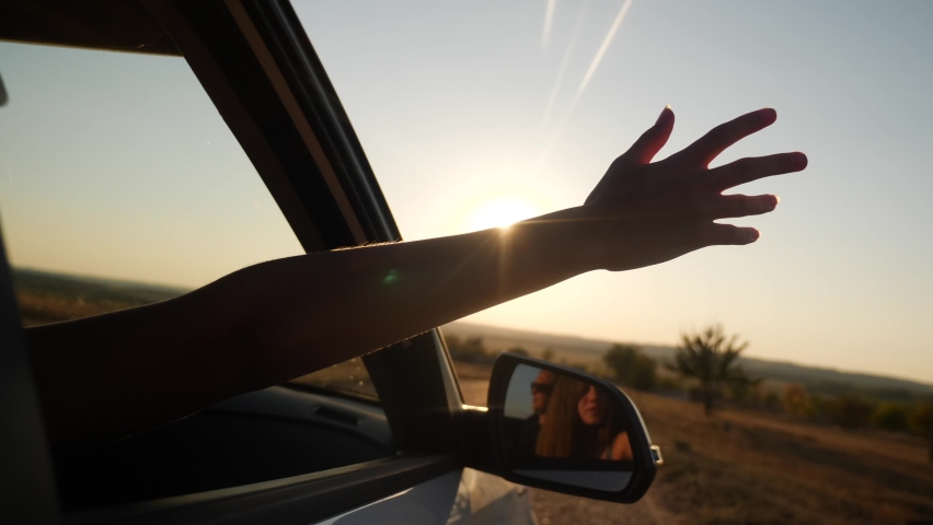 Girl stretches her hand out of the car window with sun glare at sunset. adventure journey family concept. silhouette of a girl hand from the car window on the road on a journey | Shutterstock HD Video #1064803462