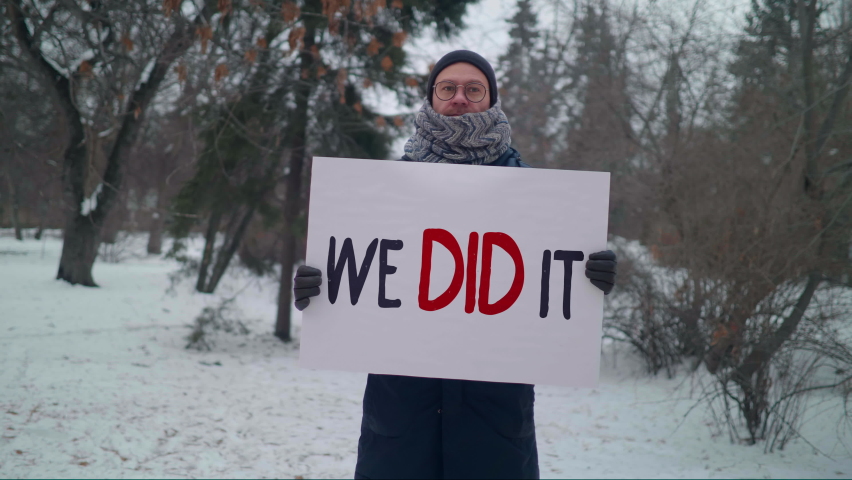 A citizen is celebrating the recent political news outside. Holding a sign that says We Did It. Showing off to his opponents. Being happy that his vote mattered. Cold weather.