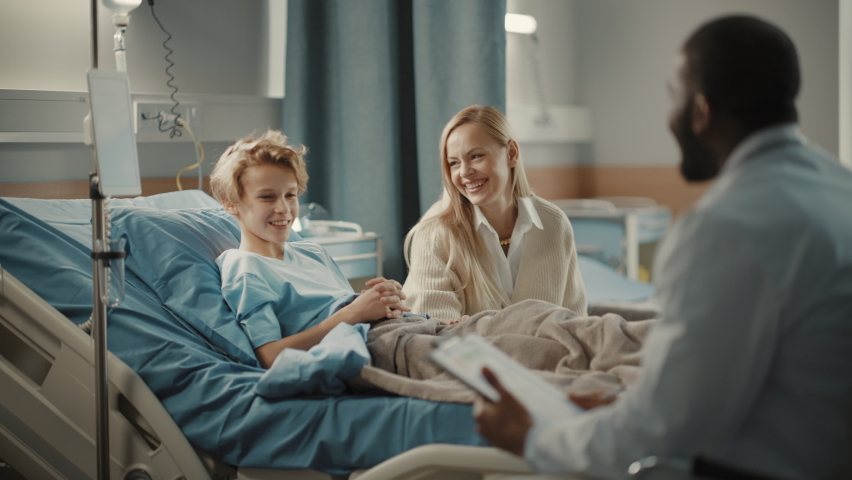 Hospital Ward: Handsome Young Boy Resting in Bed with Caring Mother Visits to Support Him, Friendly Doctor Talks, Gives Advice. Happy Smiling Patient Recovering after Sickness or Successful Surgery Royalty-Free Stock Footage #1064816728