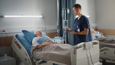Hospital Ward: Friendly Male Nurse Talks Reassuringly to Elderly Patient Resting in Bed. Doctor Uses Tablet Computer, Does Checkup, Explains Analysis, Old Man Recovering after Successful Surgery