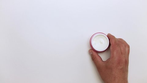 A man's hand takes a jar of cream from the table. Ointment for cosmetics. Self-care skin. Isolated video on a white background. Close-up. There is copy space. Warm, soft light. UHD.