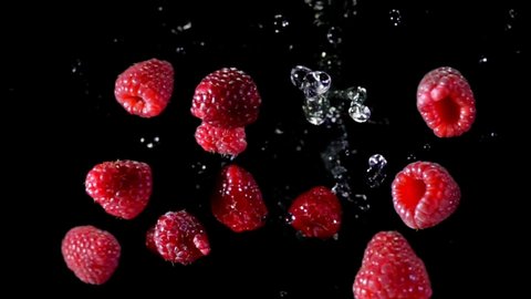 Top view of the ripe raspberries bouncing and rotating in the air with the drops of water on a black background in super slow motion.