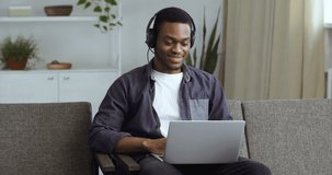 Black guy afro american businessman freelancer student teenager in headphones with laptop listening to music watching video clips enjoying song sounds singing moves dancing hands resting at home couch