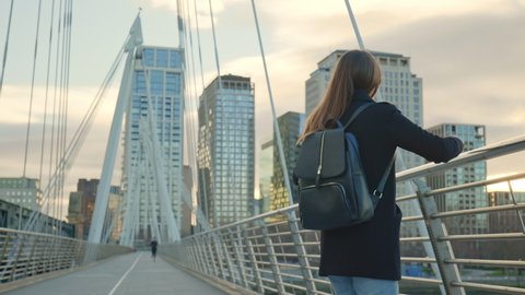 A girl tourist with backpack walking on Millennium Bridge, London in lockdown. A female in a coat during winter with no people walking in front of most famous London landmarks in slow-motion in 4K.