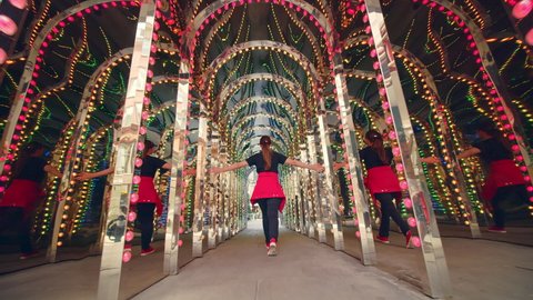 Beautiful girl walking in slow-motion in tunnel with many colorful light bulbs. Concept of a tourist enjoying local city landmarks, art and most famous places in 4K.