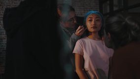 Group of girls preparing young asian woman for plastic surgery. Caucasian girl cosmetologist drawing lines on customer face before beauty treatment surgical procedure.