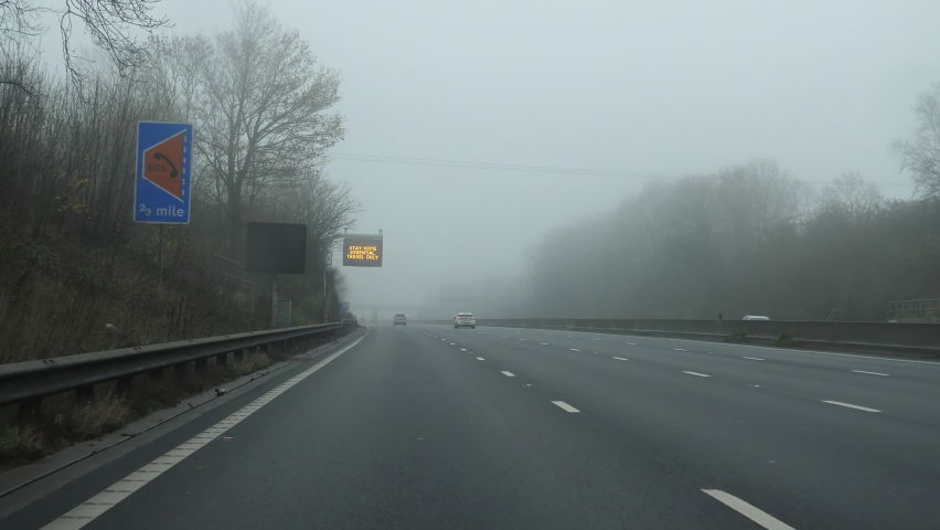 Driving highway in fog; there is a message on roadside board for drivers saying: Stay home, essential travel only. Due to coronavirus pandemic in the UK travelling has restrictions. Royalty-Free Stock Footage #1064843041