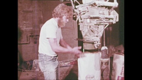 1970s: Man removes bag from underneath chute. Man dumps bag into tumbler. Cows eat from trough. Tanks of ammonia in row. Tractor pulls tank of ammonia across field.