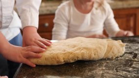 Two pair of kid hands are kneading the dough. Close up video as hands of the kids are preparing the dough for the pretzels.