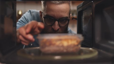 Man putting leftover dinner into microwave oven to cook. View from inside microwave of guy putting dinner in plastic container to warm. Male heating meal in oven