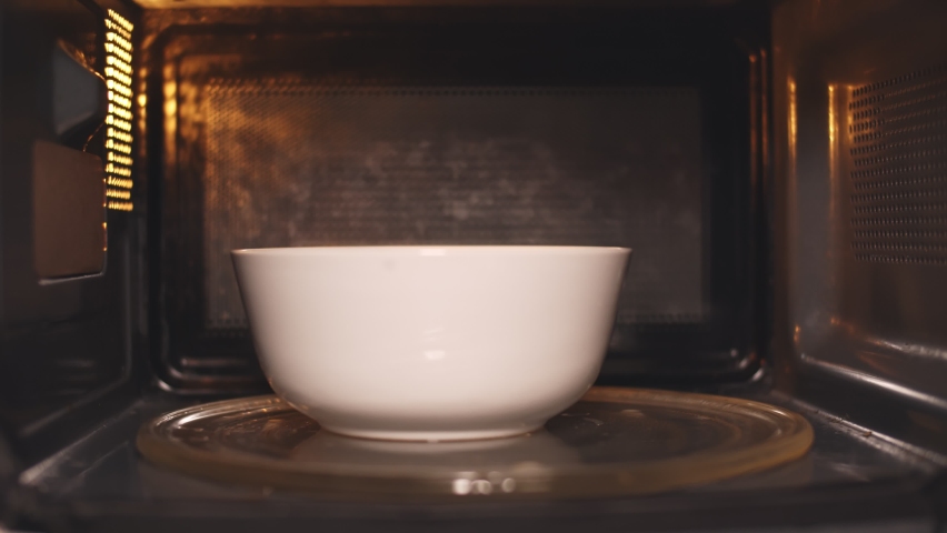 Young caucasian man heating food in microwave oven. View from inside microwave of bearded guy opening door and taking warm bowl with meal for dinner Royalty-Free Stock Footage #1064847733
