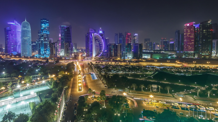 The skyline of the West Bay area from top in Doha timelapse, Qatar. Illuminated modern skyscrapers aerial view from rooftop at night. Parks and traffic on the road